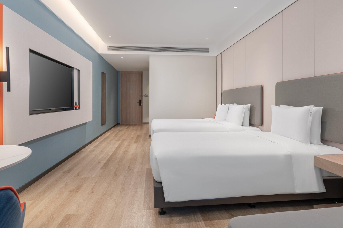 A modern hotel room with a large bed, bedside tables, a TV, and a seating area.