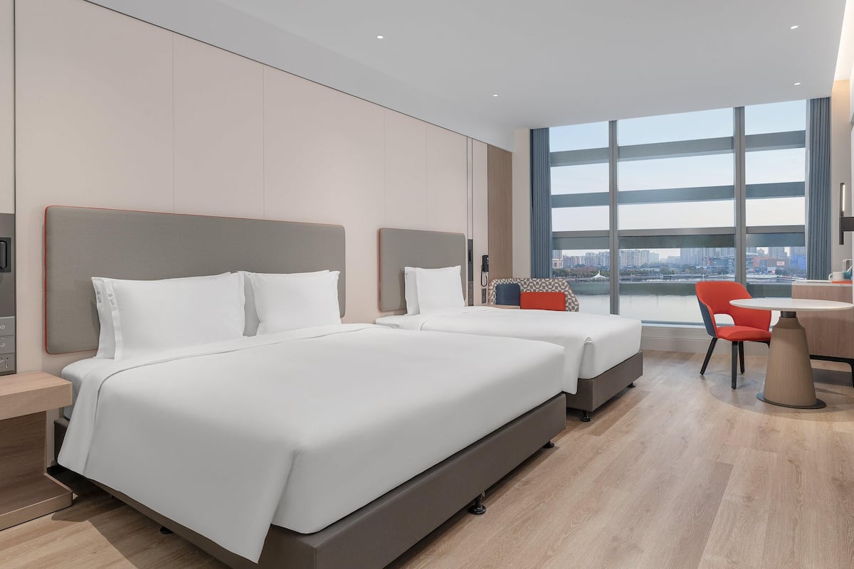 Ein modernes Hotelzimmer mit zwei Betten, einem Schreibtisch und einem großen Fenster mit Blick auf die Stadt.
