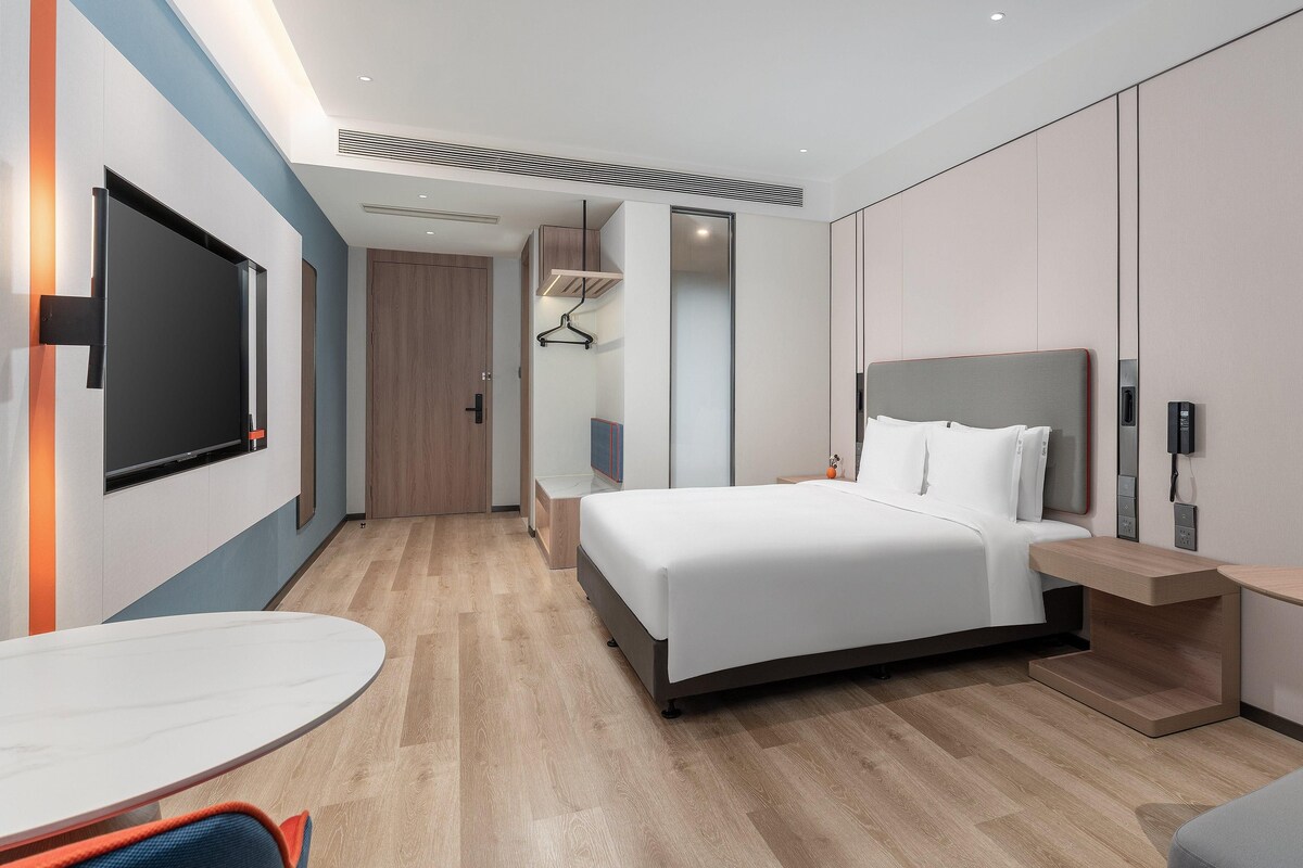 A modern hotel room with a bed, bedside table, and a TV.