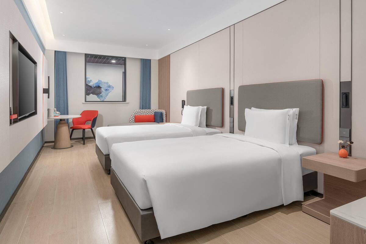 Ein modernes Hotelzimmer mit zwei Betten, einem Schreibtisch und einem Stuhl.