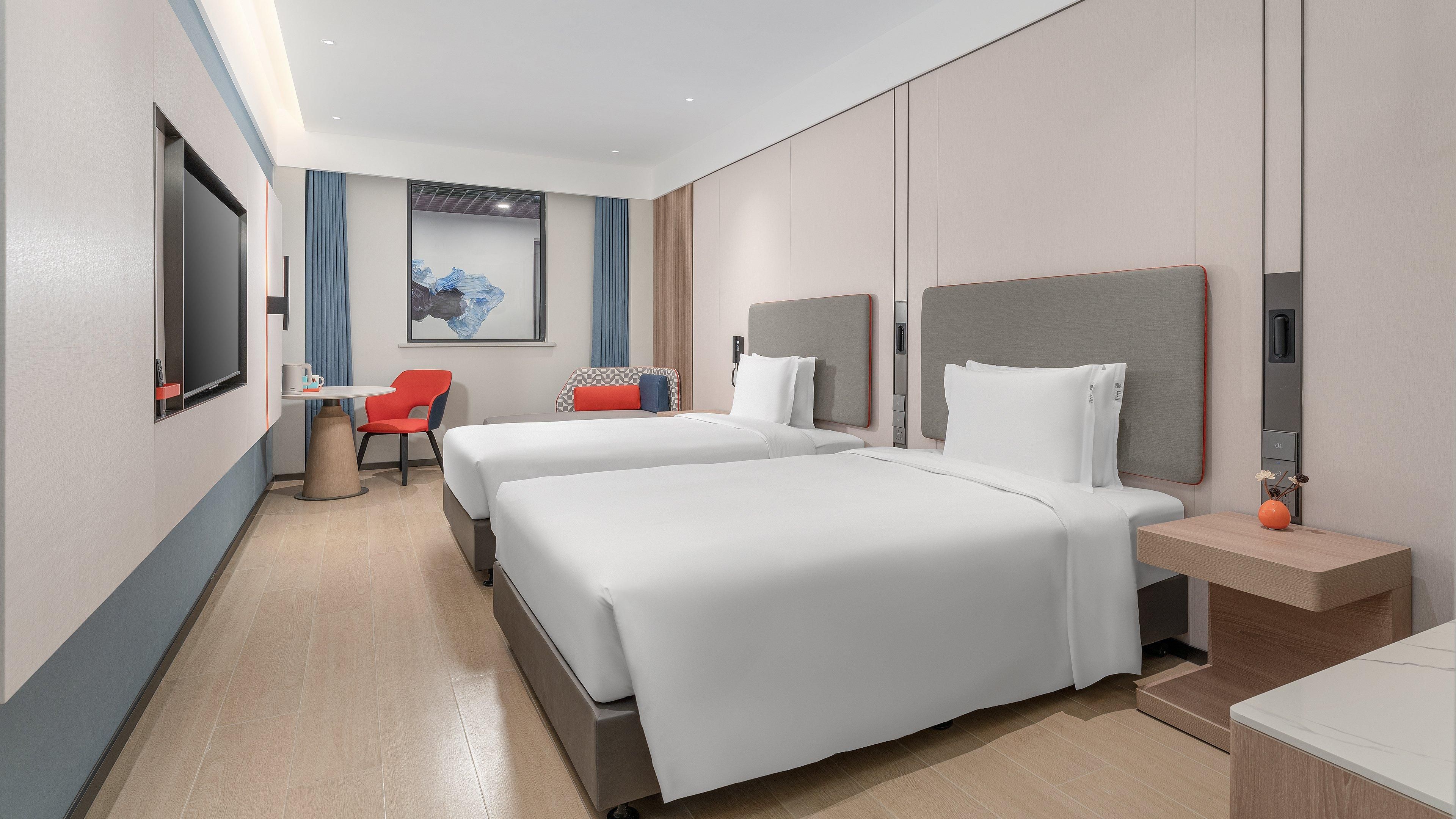A modern hotel room with two beds, a desk, and a chair.