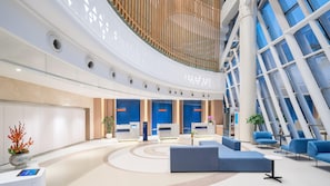 A modern lobby with a curved ceiling, blue seating areas, and a reception desk.