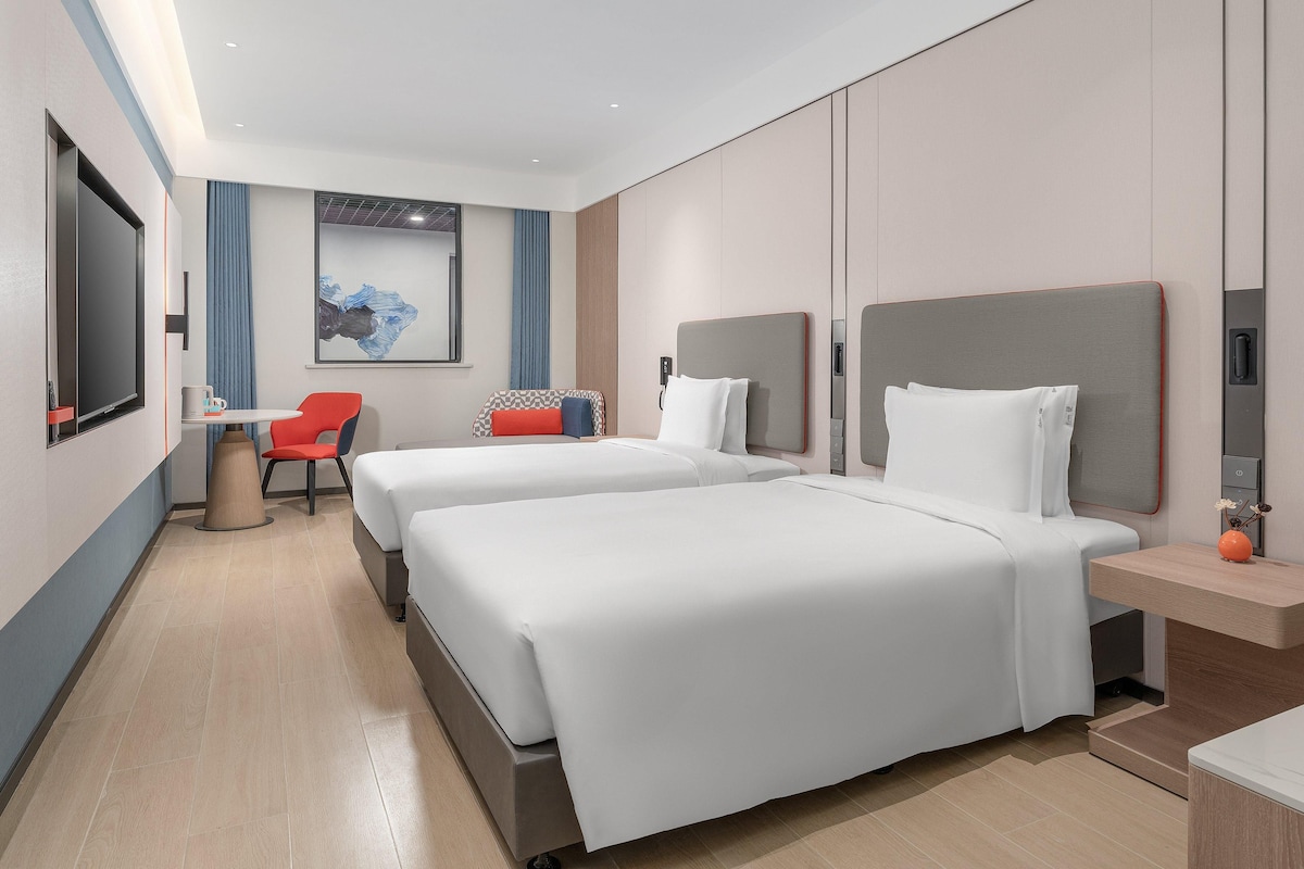 A modern hotel room with two beds, a desk, and a chair.