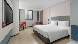 A modern hotel room with a large bed, a desk with a chair, a television, and a window with a view of trees.