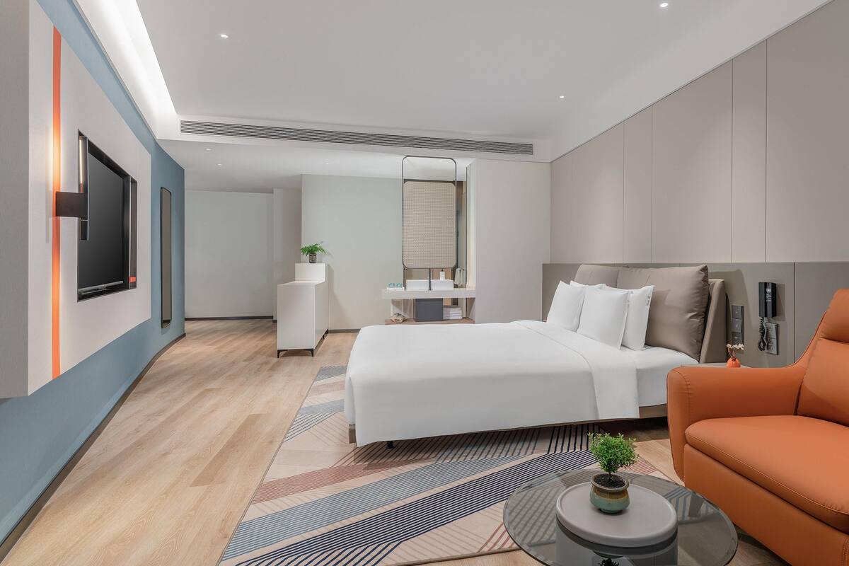 Ein modernes Hotelzimmer mit einem großen Bett, einer Couch, einem Fernseher und einem im Hintergrund sichtbaren Badezimmer.