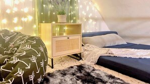 A cozy tent-style room with a bed, a small bedside table with a lamp, and fairy lights. - Charming 3-bedroom cabin in with AC, spa, game room, firepit & EV charger  (Old Station)