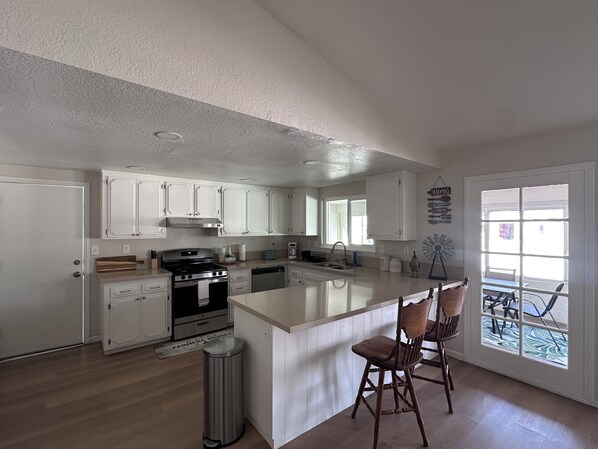 A modern kitchen with white cabinets, a central island, and a dining area with two wooden chairs.