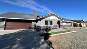 A single-story house with a stone chimney, a garage, and a well-maintained lawn. - 3-bdrm house in charming Apple Valley w/ WiFi, AC, encl'd patio, & large yard.  (Apple Valley)