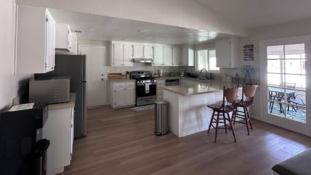 A modern kitchen with white cabinets, a central island with bar stools, a built-in oven, and a refrigerator. - 3-bdrm house in charming Apple Valley w/ WiFi, AC, encl'd patio, & large yard.  (Apple Valley)