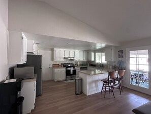A modern kitchen with white cabinets, a central island with bar stools, a built-in oven, and a refrigerator.
