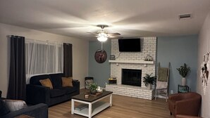 A living room with a fireplace, a ceiling fan, a television mounted on the wall, and a sofa. - 3-bdrm house in charming Apple Valley w/ WiFi, AC, encl'd patio, & large yard.  (Apple Valley)