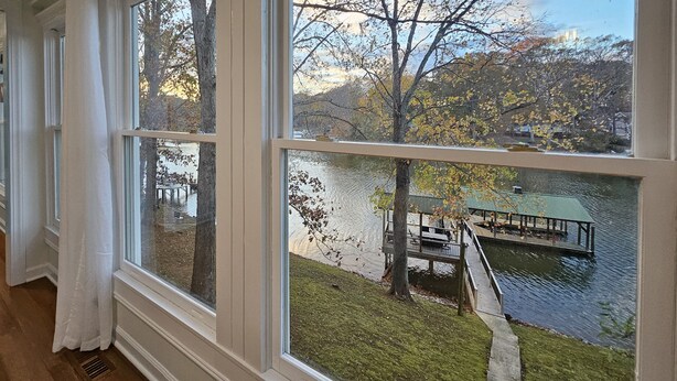 A room with large windows overlooking a lake, a dock, and a grassy area with trees. - The Nest, 2 Houses Next Door on Lake Norman (Sherrills Ford)