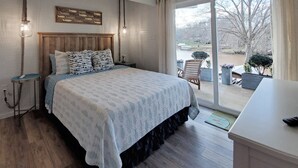 A bedroom with a large bed, wooden headboard, and a view of a park through a sliding glass door. - The Nest, 2 Houses Next Door on Lake Norman (Sherrills Ford)