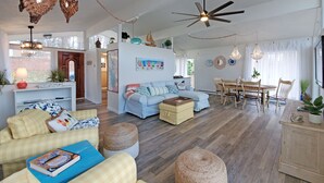A spacious living room with a sofa, coffee table, and ottoman, a dining area with a wooden table and chairs, and a kitchen area with a stove and cabinets. - The Nest, 2 Houses Next Door on Lake Norman (Sherrills Ford)