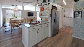A modern kitchen with white cabinetry, a stainless steel refrigerator, and a dining area with wooden chairs and a table. - The Nest, 2 Houses Next Door on Lake Norman (Sherrills Ford)