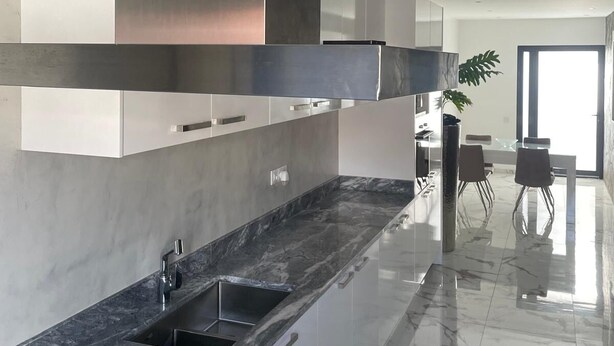 A modern kitchen with a gas stove, stainless steel range hood, and a marble countertop.
