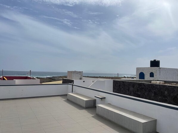 A rooftop terrace with a view of the sea and a distant mountain.