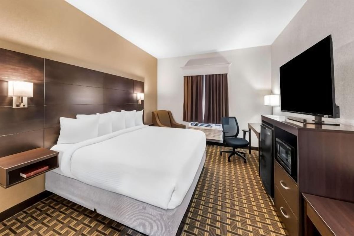 Une chambre d’hôtel avec un grand lit, un bureau avec un ordinateur, une télévision et une chaise.
