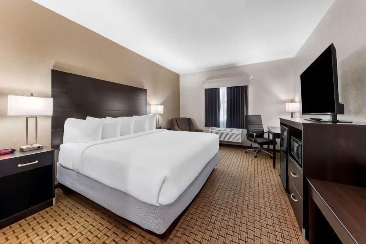 A hotel room with a large bed, a desk with a flat-screen TV, a chair, and a dresser.
