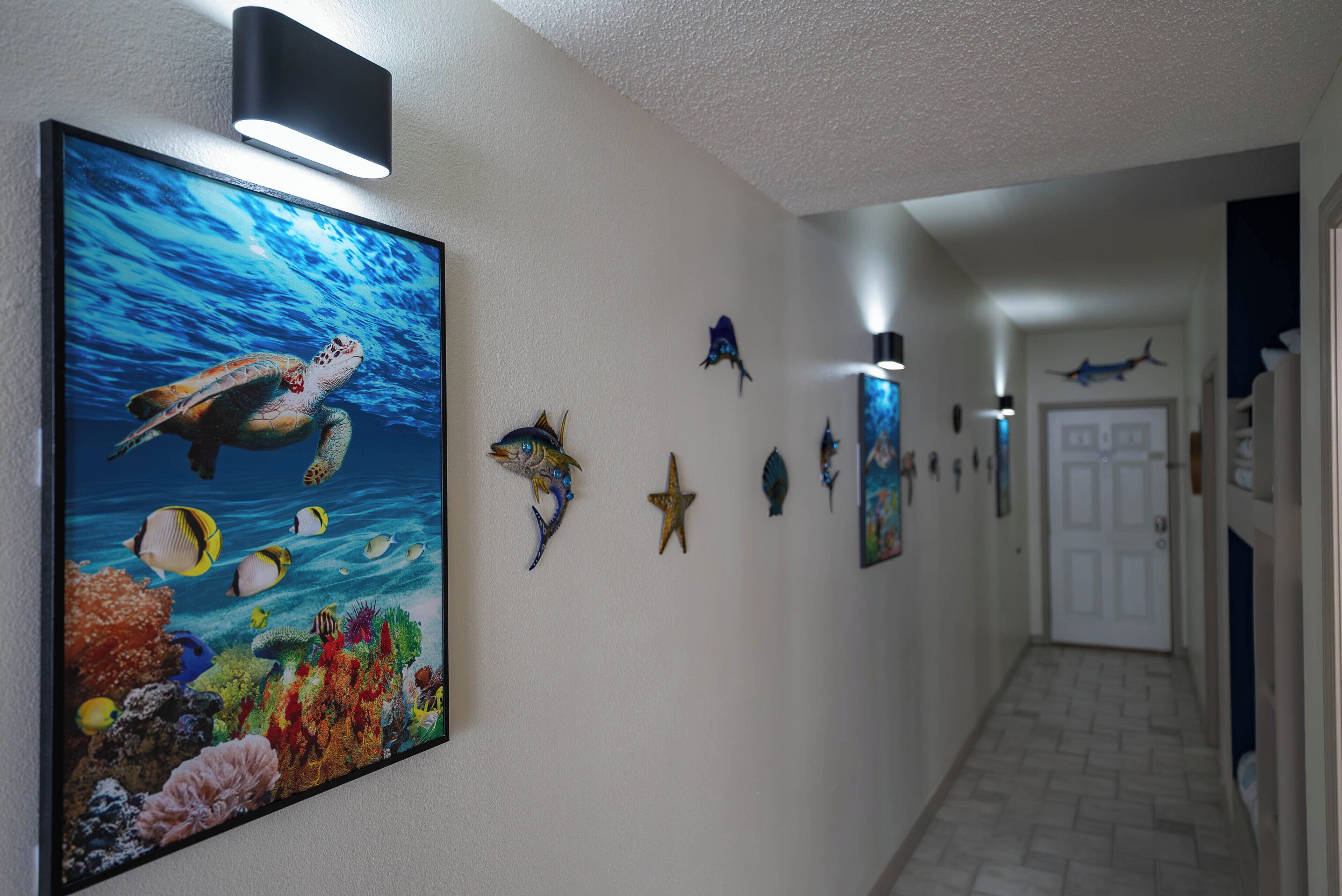 A hallway with a large marine-themed painting, various wall decorations including fish and starfish, and a door at the end.