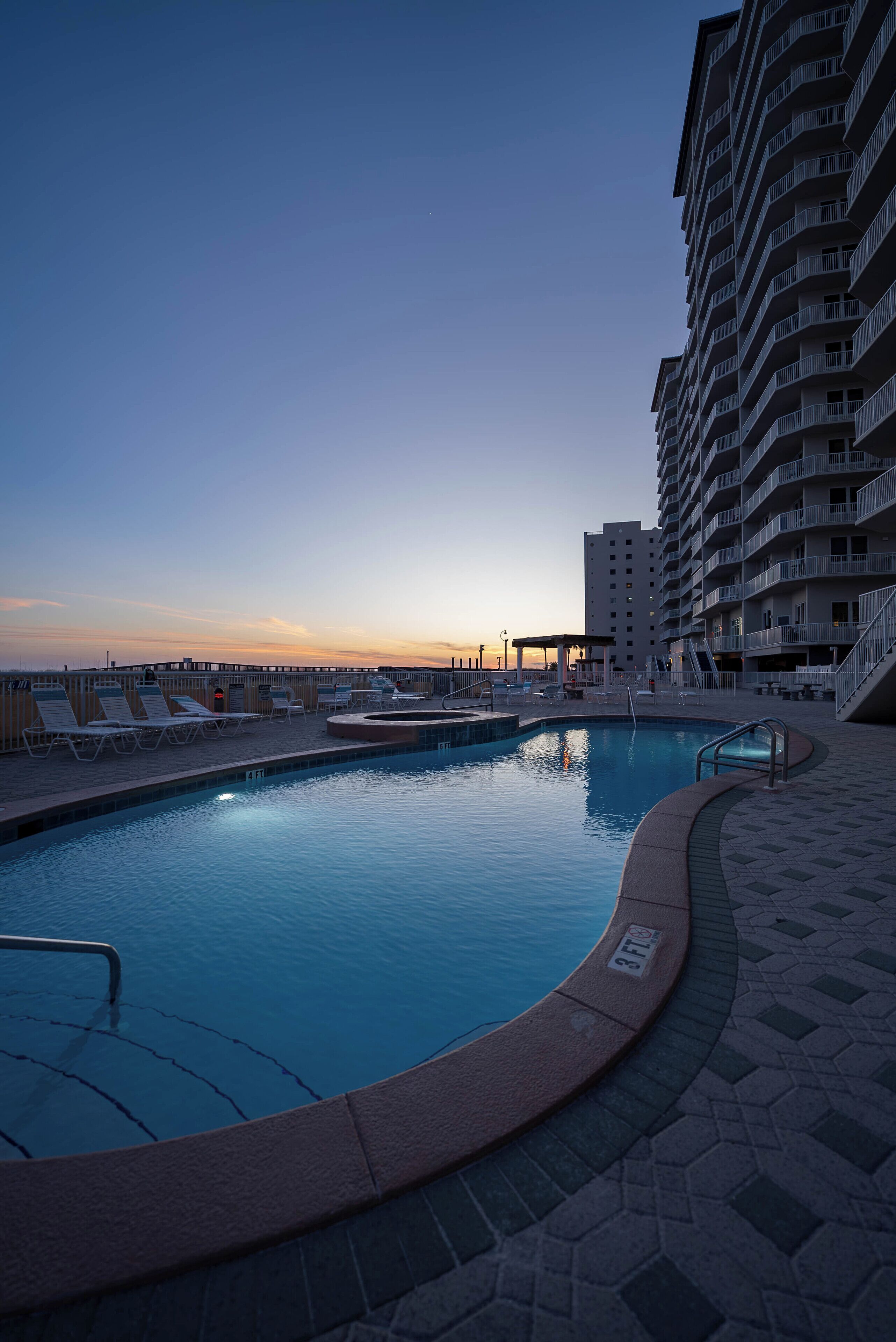 A pool area with lounge chairs and a view of a high-rise building.
