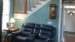 A living room with a black leather sofa, a wooden staircase, and a clock on the wall.