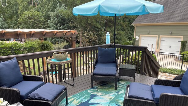 A deck with wicker furniture, a blue umbrella, and a tropical leaf-patterned rug.
