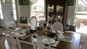 A dining table set with white chairs, a wooden table, and various table settings including plates, glasses, and a decorative centerpiece.