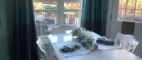 A dining area with a white table set for four, surrounded by white chairs.