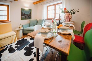 A dining area with a wooden table set for two, a sofa, a small side table, and a decorative vase with flowers. - Historic Cottage in Old Town - for 6 guests (Bad Tölz)