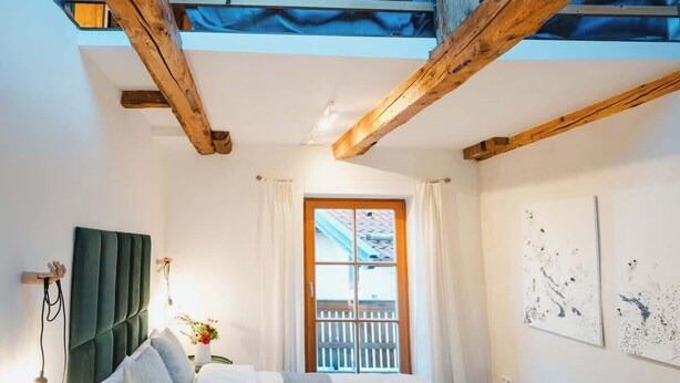 A bedroom with a bed, a window, a view of the outside, and a wooden ceiling structure.