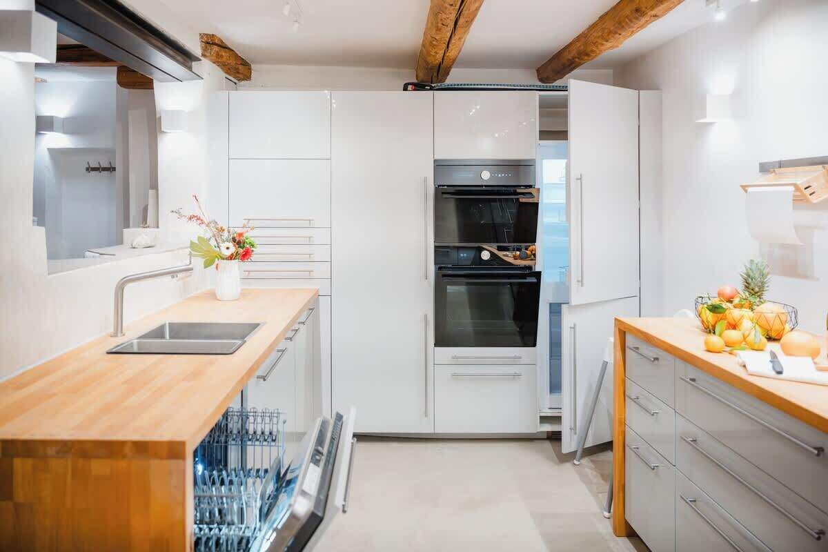 Une cuisine moderne avec des meubles blancs, un plan de travail en bois et un lave-vaisselle encastré.