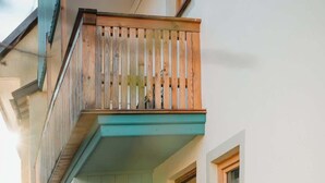 A cozy outdoor seating area with a wooden bench and cushions, a teal door, and a small window.