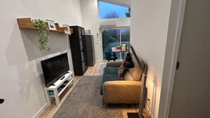 A compact living space with a TV, sofa, and a small dining area with a table and chairs.