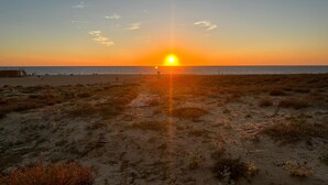 A beach with a sunset, sandy dunes, and a clear sky.