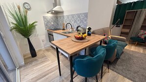 A modern kitchen with a wooden table, teal chairs, and a fruit bowl.