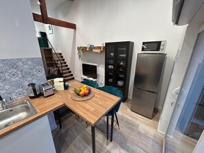Une cuisine de taille réduite avec une table en bois, un panier de fruits, un four à micro-ondes et un réfrigérateur.