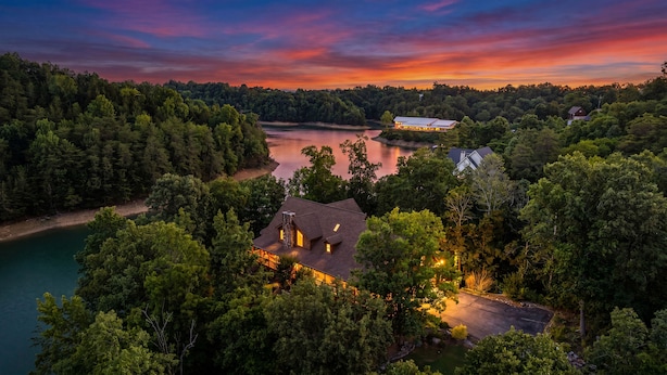 Ein Haus, umgeben von dichtem Wald, mit Blick auf einen See und einen Sonnenuntergang.