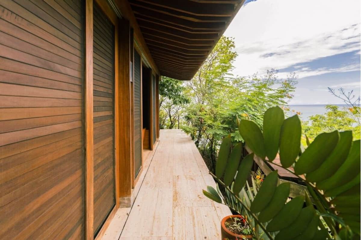 A wooden deck with a view of the ocean, surrounded by greenery.