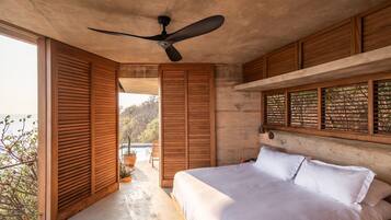 A bedroom with a large bed, wooden shutters, a ceiling fan, and a view of the outdoors.