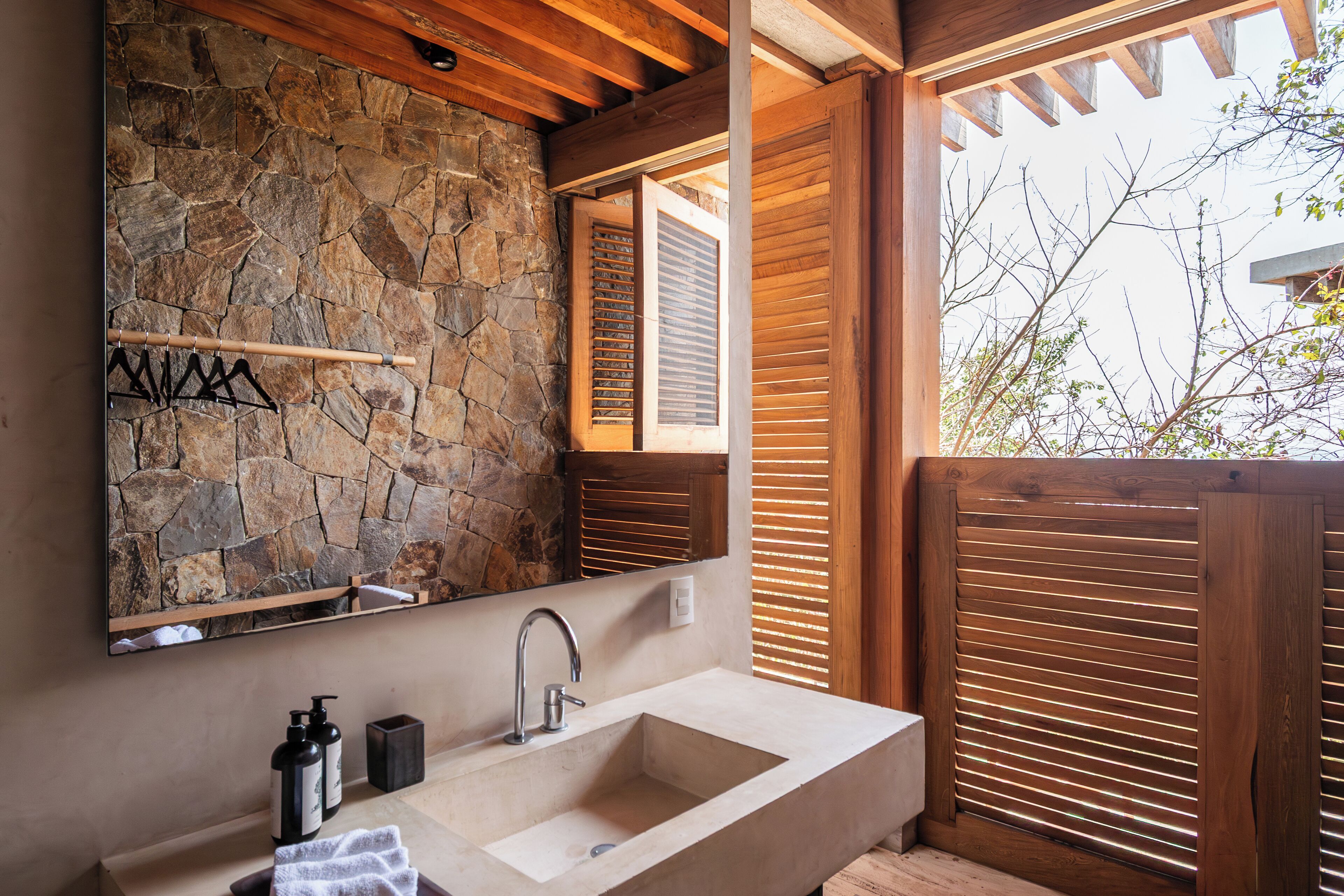 A bathroom with a stone wall, wooden ceiling beams, a large mirror, a sink, and wooden shutters.