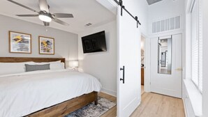 A bedroom with a bed, a ceiling fan, a mounted TV, and a door leading to a bathroom. - Cozy 1-bedroom condo, fitness room in brilliant Atlanta-Ponce City Market Area (Atlanta)