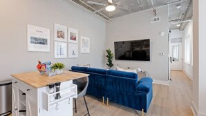 A modern living room with a blue sofa, a wooden coffee table, and a flat-screen TV mounted on the wall. - Cozy 1-bedroom condo, fitness room in brilliant Atlanta-Ponce City Market Area (Atlanta)