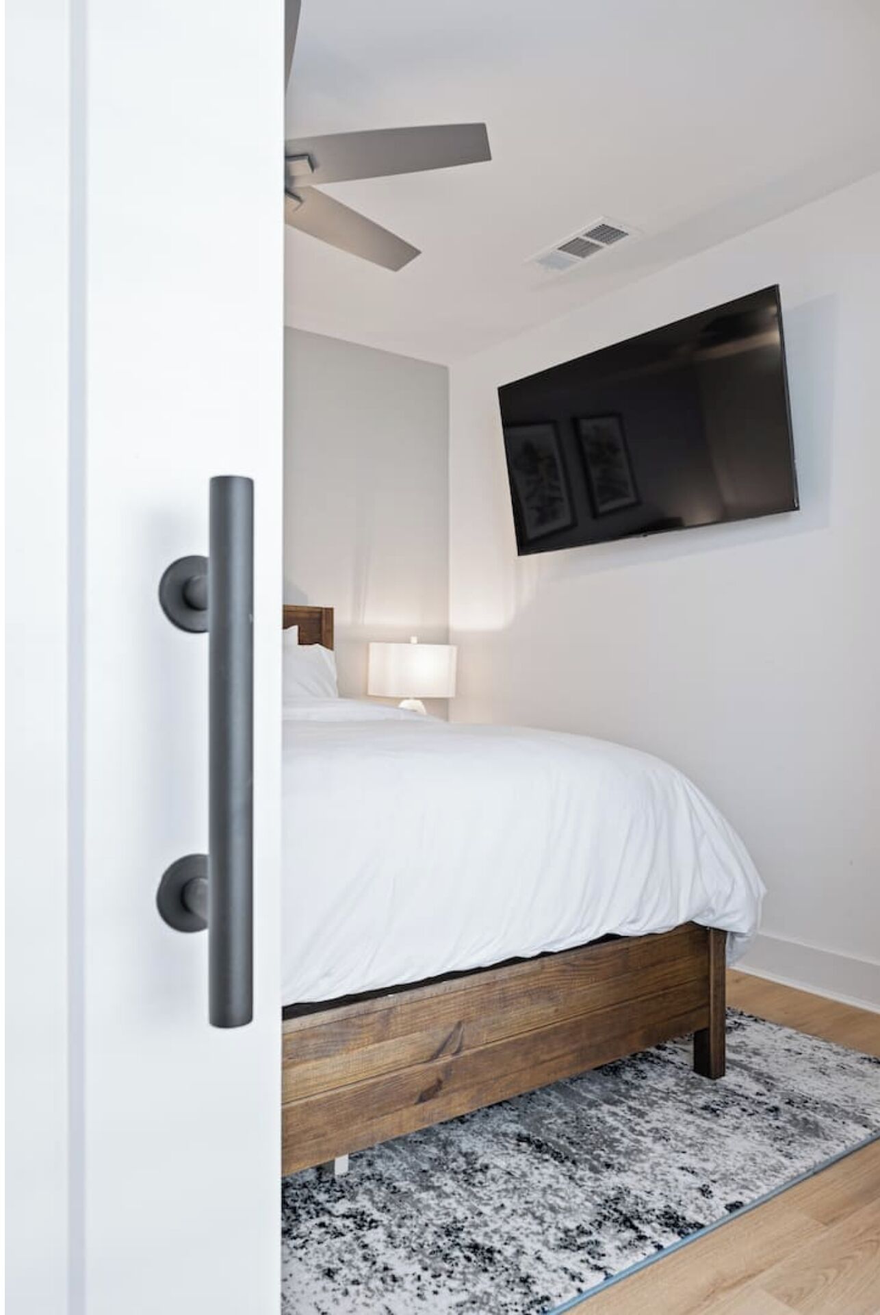 A modern bedroom with a bed, a mounted TV, and a door with a handle.