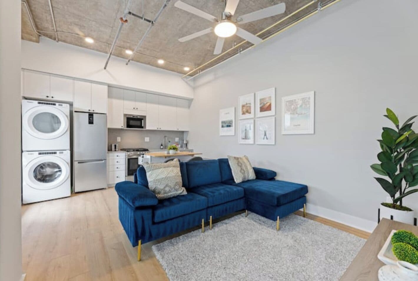 Eine moderne Wohnung mit Küche, einem blauen Ecksofa und einem Deckenventilator.