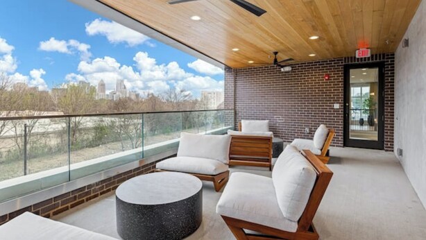 A modern outdoor seating area with a view of the city skyline, featuring a mix of wooden and brick elements, and a glass railing. - Cozy 1-bedroom condo, fitness room in brilliant Atlanta-Ponce City Market Area (Atlanta)