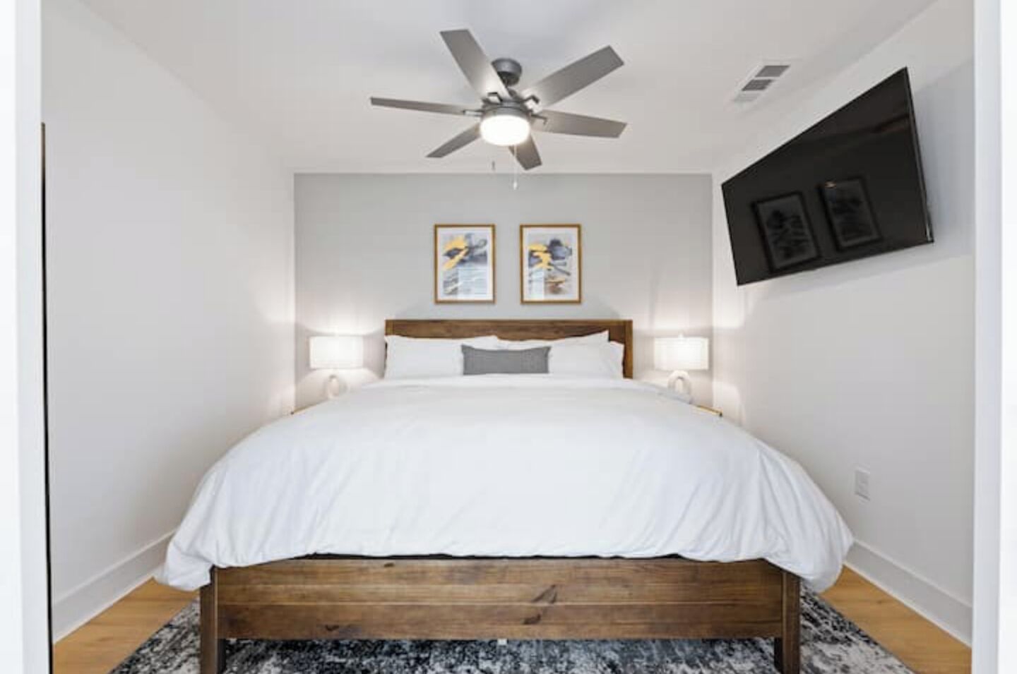 Une chambre à coucher avec un lit en bois, un ventilateur de plafond, deux lampes fixées au mur et deux tableaux encadrés.