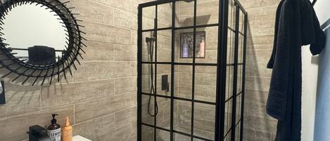 A modern bathroom with a glass shower enclosure, a white sink, and a round mirror with a black frame.