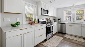 A modern kitchen with white cabinetry, stainless steel appliances, and a large window providing natural light.