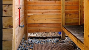 A wooden sauna with a sloped roof, a wooden bench, and a pebble-covered floor.